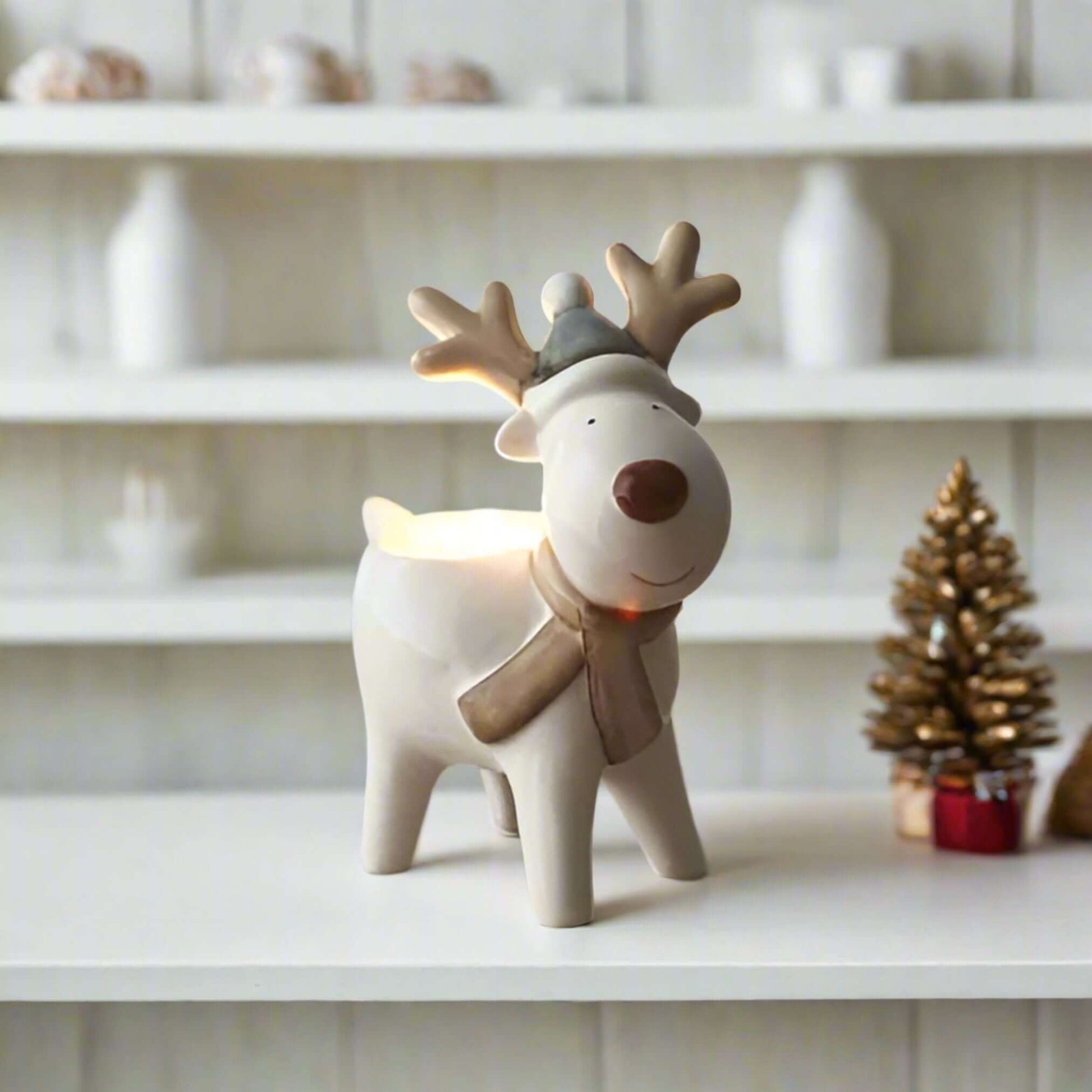Tealight Holder Reindeer with Hat and Scarf.Add a touch of festive cheer to your home with this charming ceramic reindeer tealight holder. Its simplistic design, featuring neutral tones and a bold cute red nose, makes it a versatile piece that complements